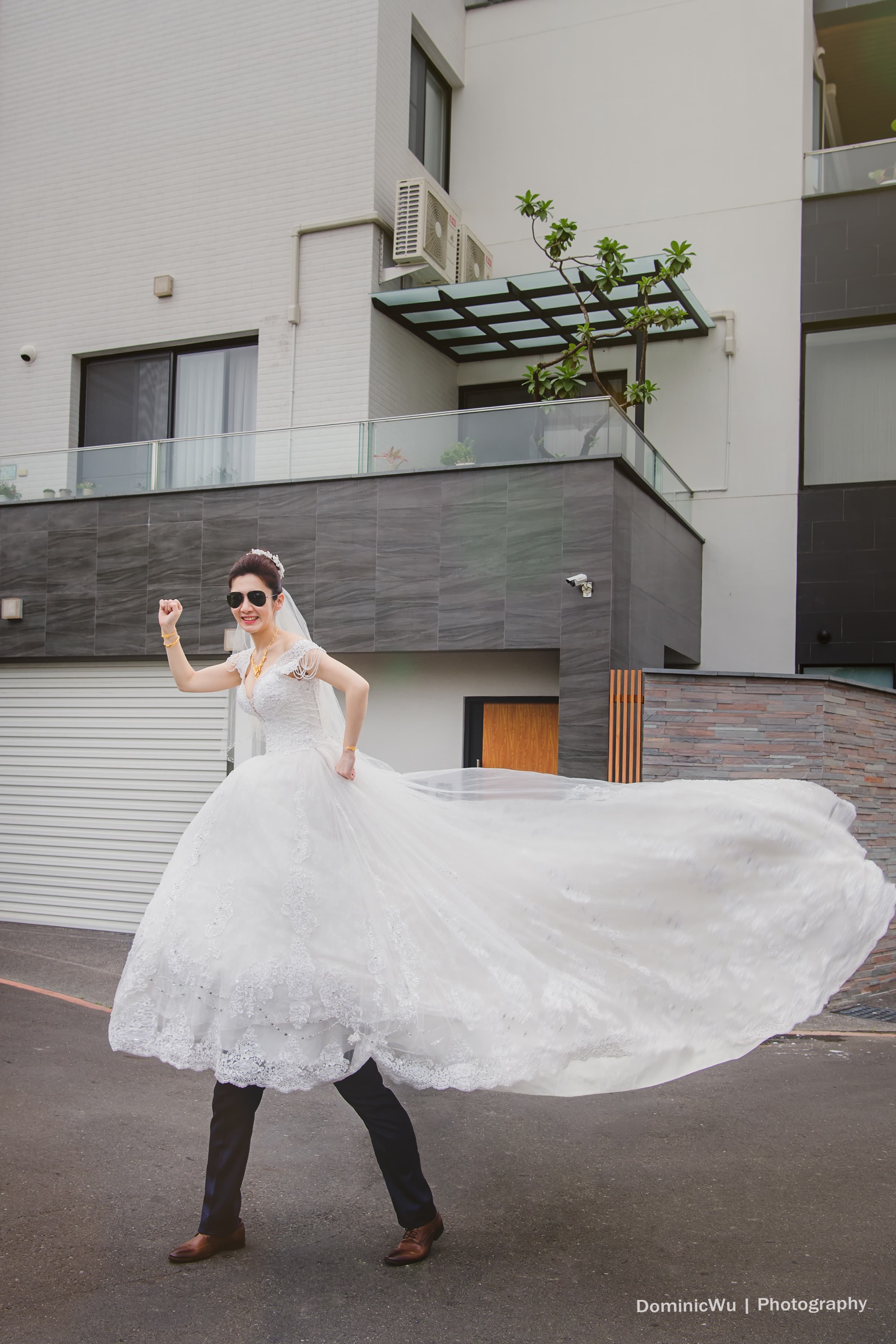 這張照片是一個穿著婚紗的女性，她舉起手，正在微笑。她身穿白色的婚紗，裙擺很大，向外伸展，幾乎佔據了整個照片畫面。她看起來非常快樂，彷彿在享受婚禮的喜悅。