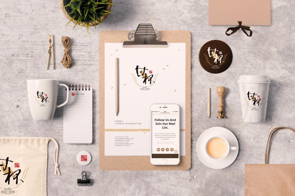 這張照片是一張展示茶品牌設計的桌面上，以木質色調為主，並有杯子、筆記本、手機等物品，突顯品牌簡潔自然的風格。