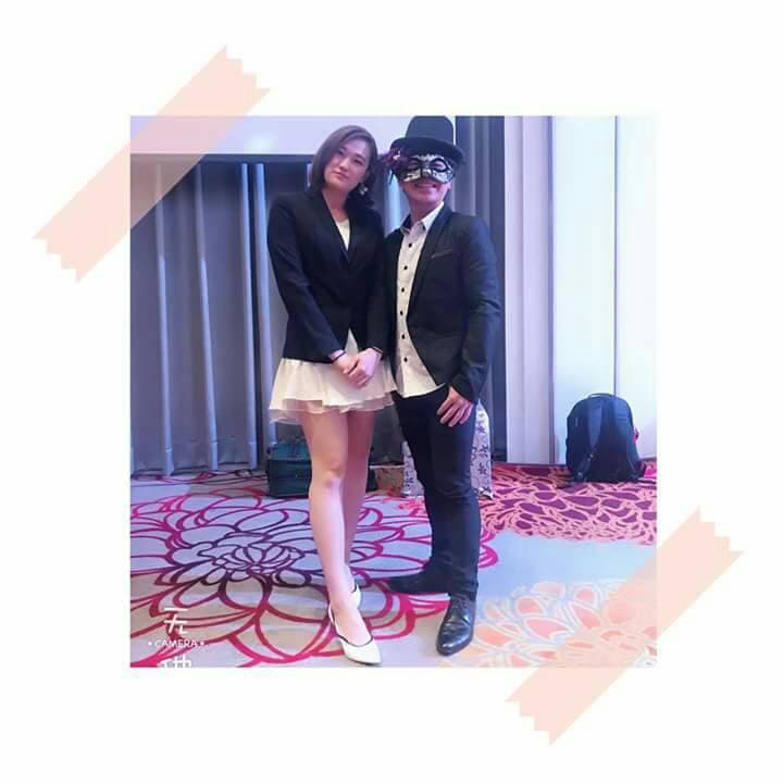 這張「兩個穿著正式服裝的人站在一起」的照片是，一個女人穿著白色短裙和黑色外套，另一個男人穿著黑色西裝和麵具。