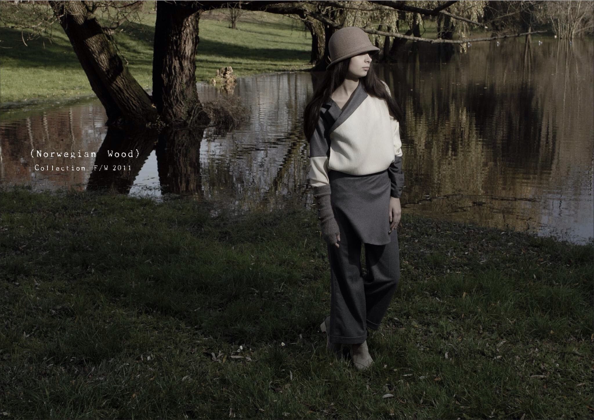 這張「」的照片是一個穿著灰色外套和帽子,站在湖邊的女子。