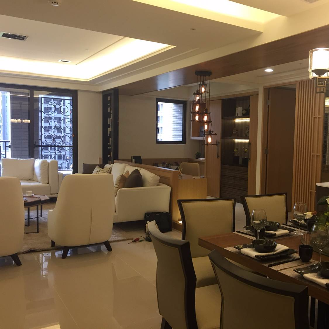 這張「現代風格客廳」的照片是,有著木質天花板和白色沙發,旁邊擺放著黑色的咖啡桌,對面是餐廳,擺著木質餐桌和白色皮革餐椅,以及一盞吊燈。