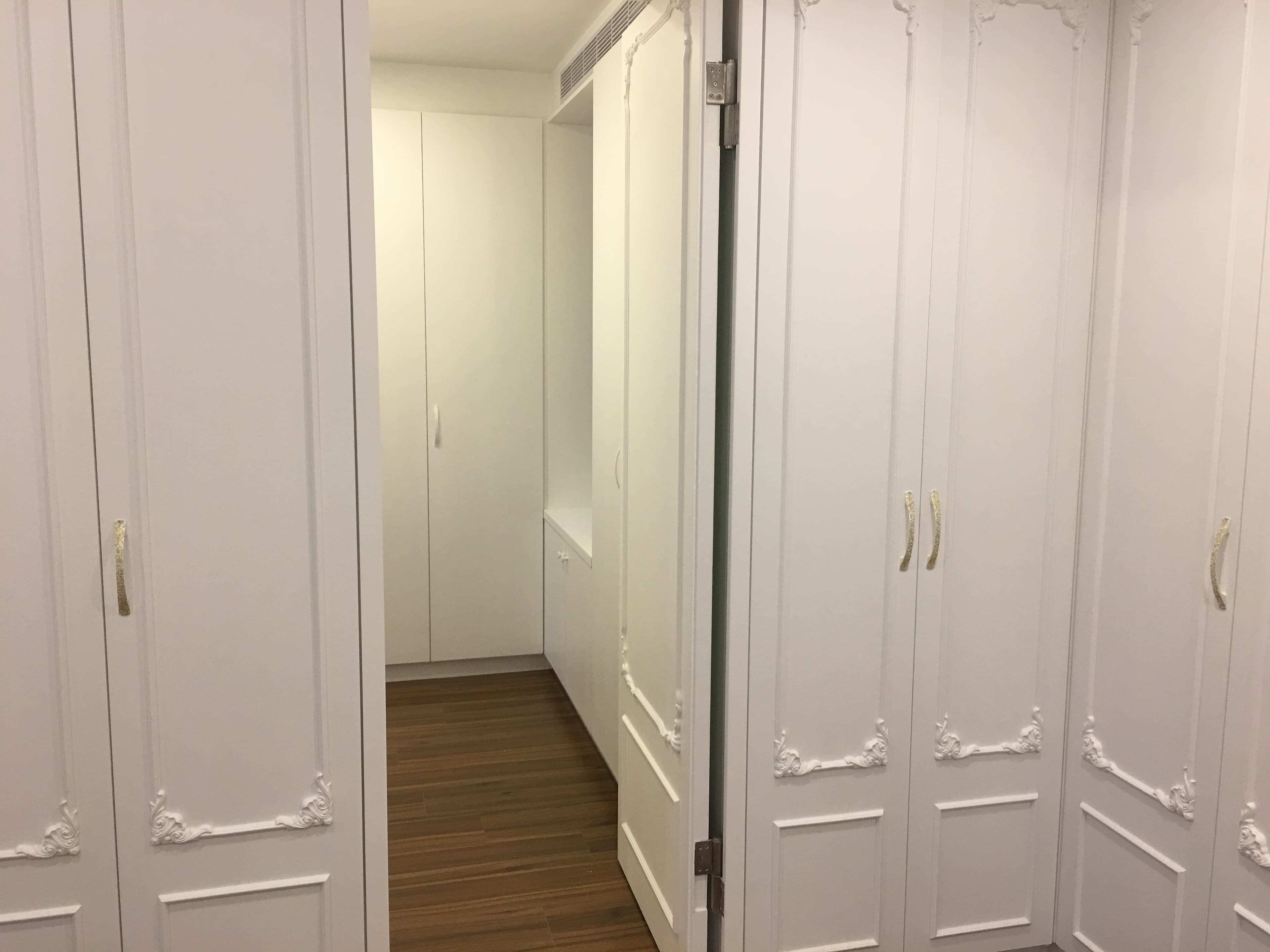 這張照片是一間白色衣櫃，櫃門上有精緻的雕刻，配上金色把手，展現出優雅的風格。