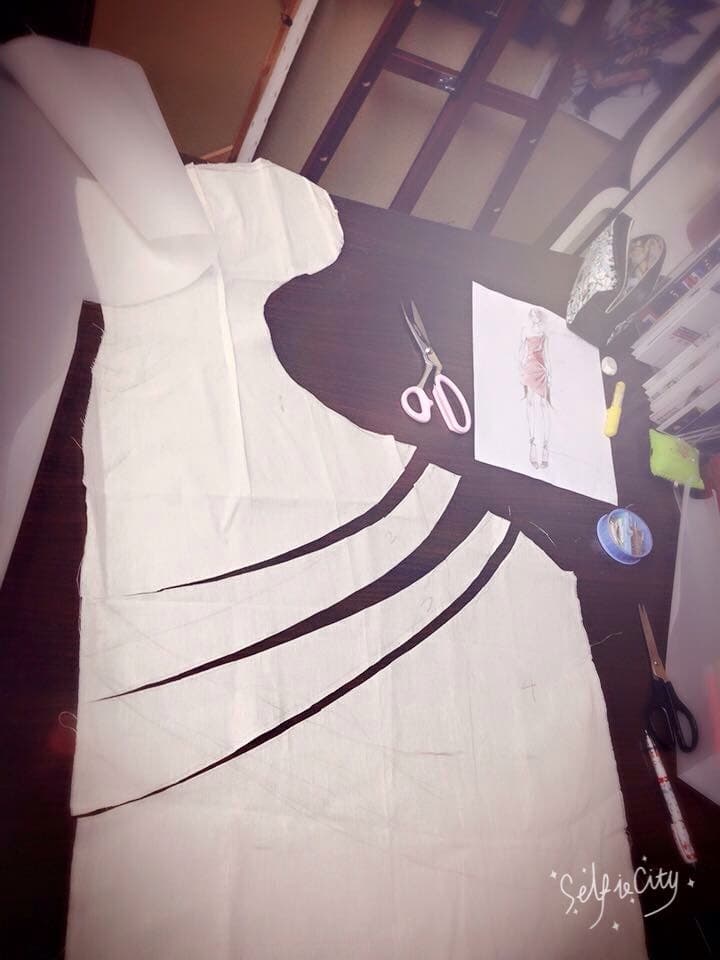 這張「裁縫」的照片是一張白色的布料,上面有黑色的線條,旁邊放著一把剪刀,還有其他裁縫工具。