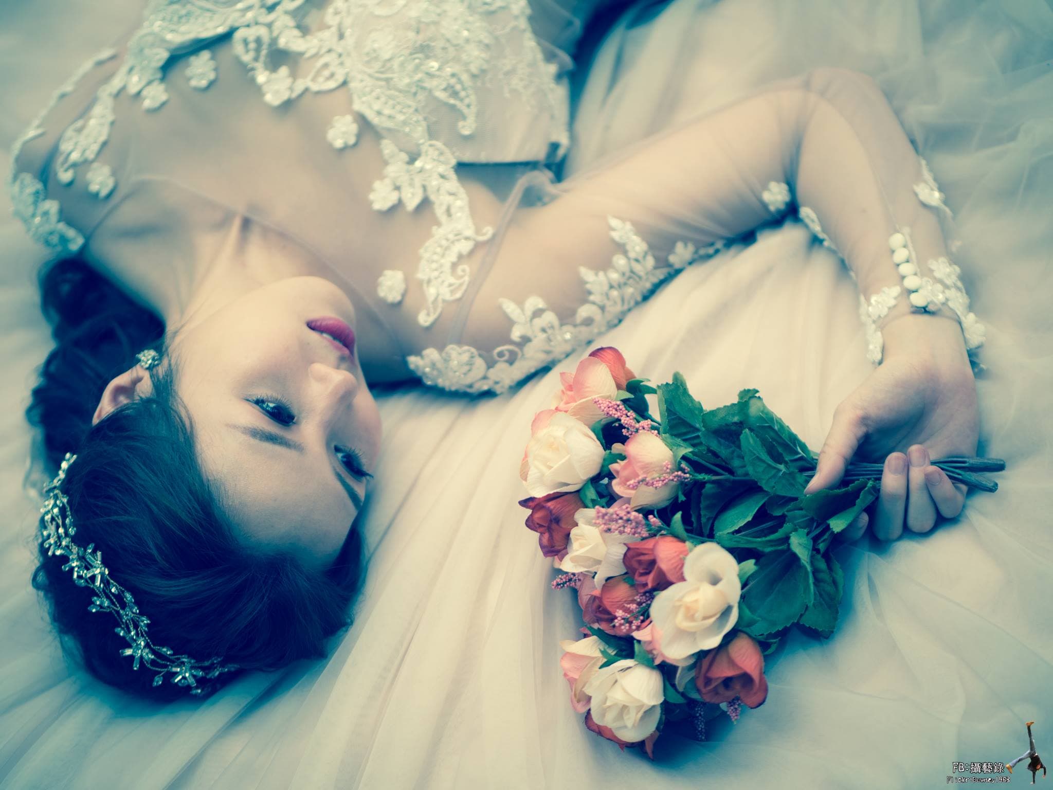 這張照片是一位美麗的女性躺在床上，她穿著一件婚紗，手上拿著一束美麗的玫瑰花。