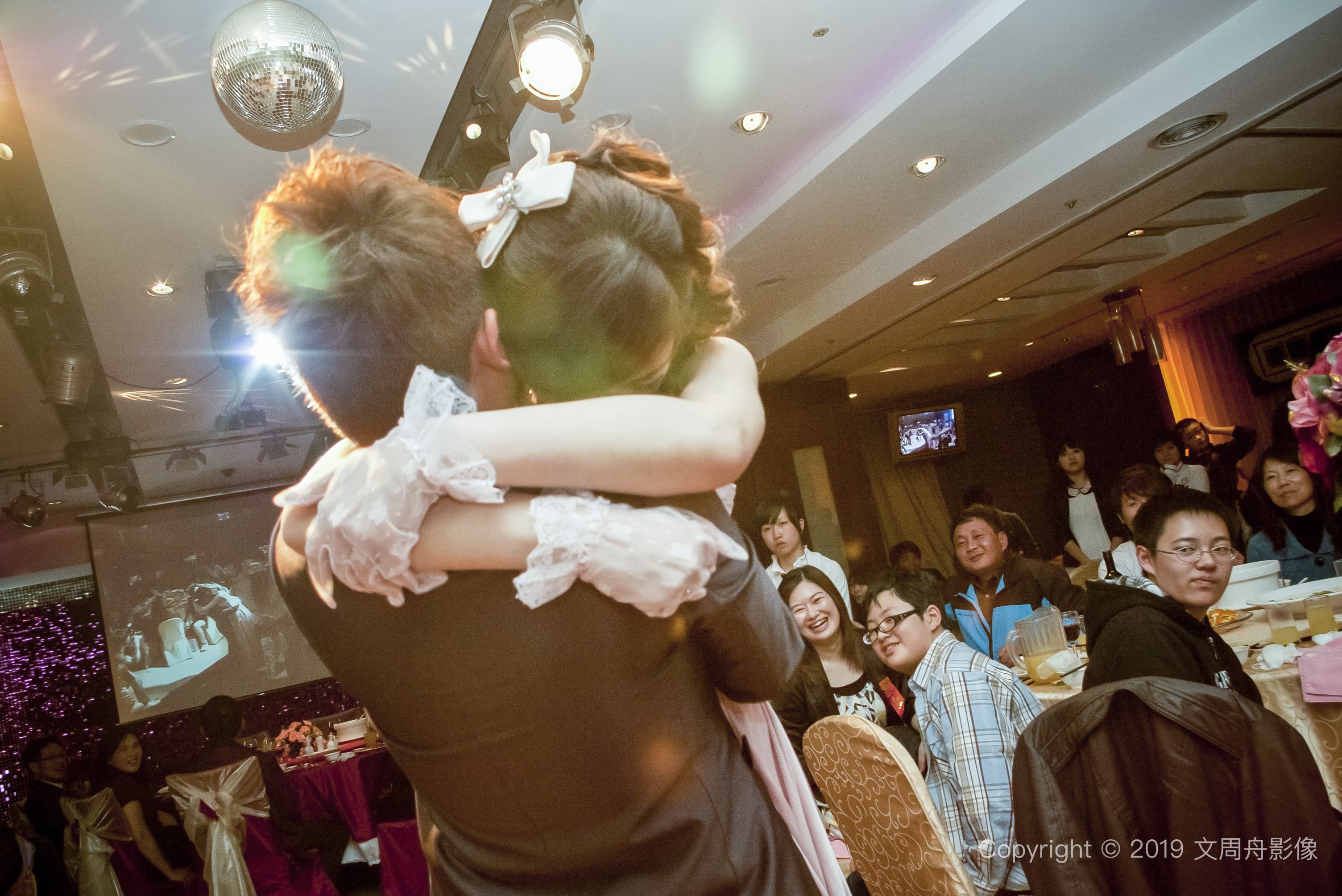 這張照片是一對新人正在擁抱，新郎穿著西裝，新娘穿著白色婚紗，他們看起來非常幸福。