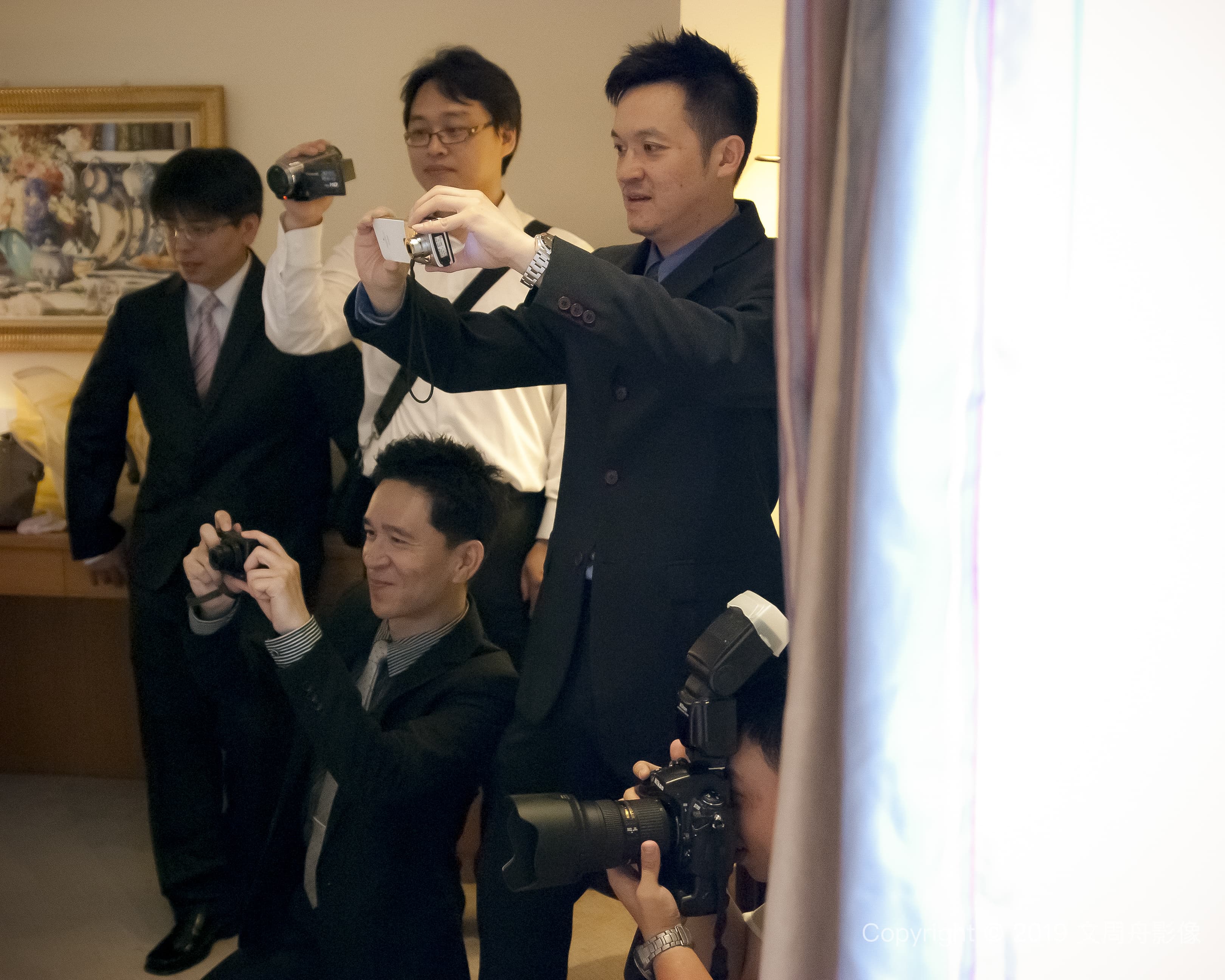 這張照片是幾個男人在室內拍照片。其中一個男人站在中間，他穿著西裝，拿著照相機，似乎是正在指導大家怎麼拍照。