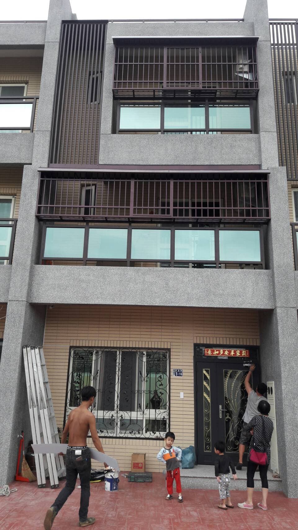 1) 照片顯示一棟三層樓的建築，外觀為水泥灰，建築物的窗戶上裝有鐵窗