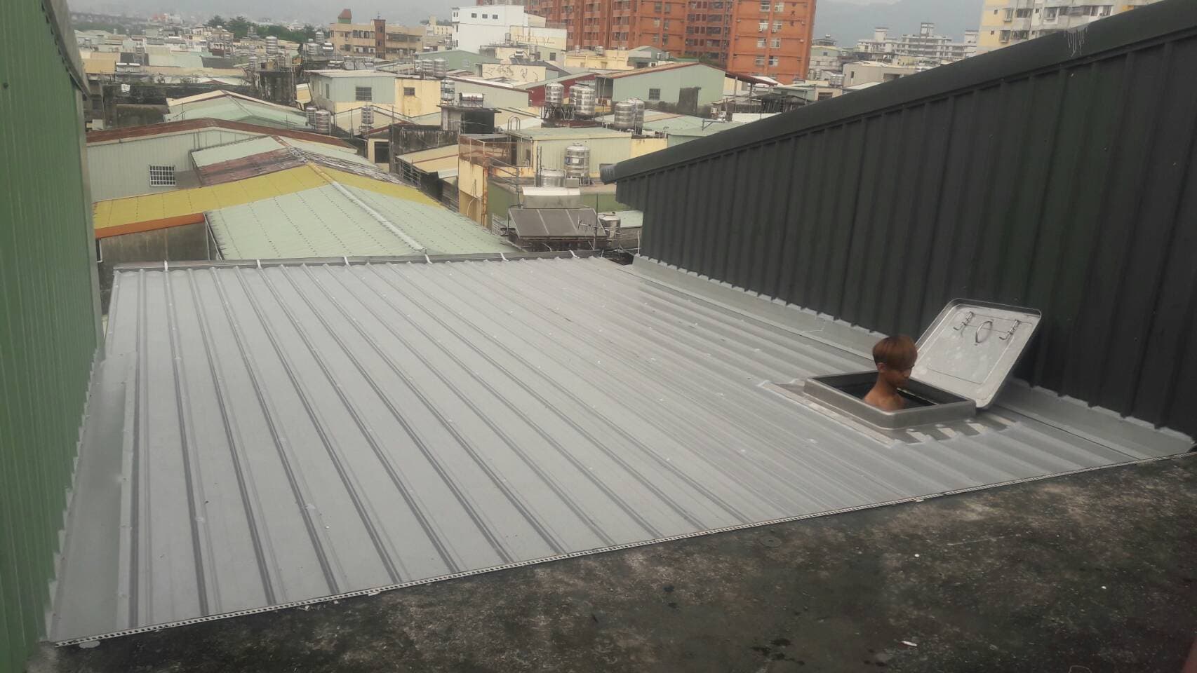 1. 照片顯示一個灰色屋頂，屋頂上有一個方形天窗，天窗裡有一個穿著白色衣服的人