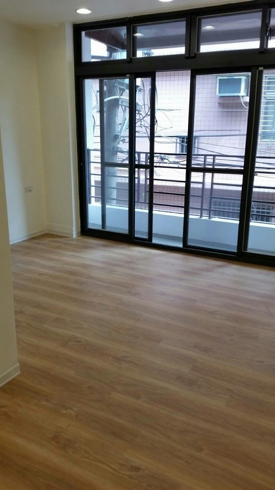 1) 照片顯示一個有著木紋地板的房間，房間中央有一扇大型的落地窗，窗外可以看到綠色的樹木和建築物