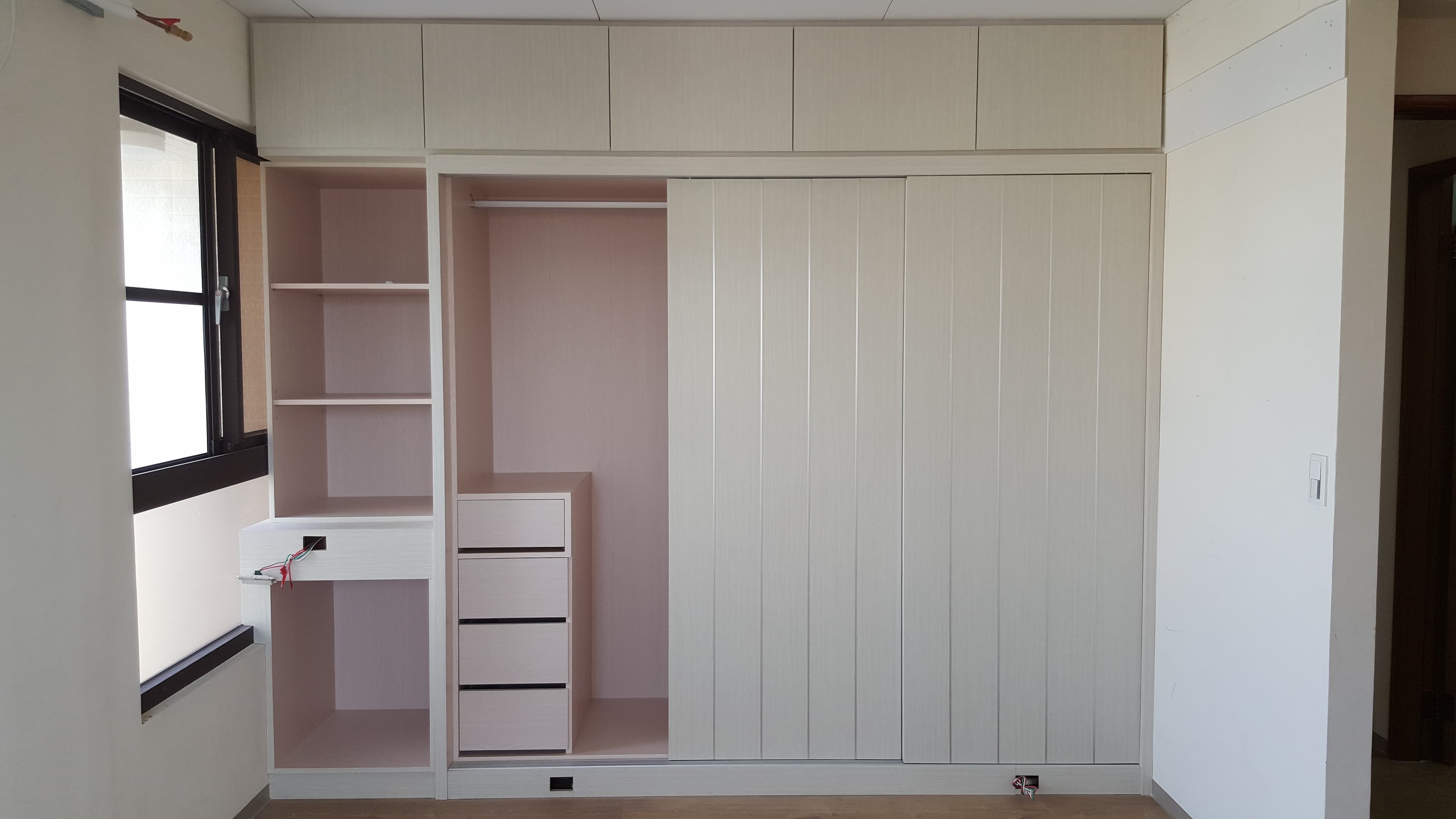 1) 照片顯示一個白色衣櫃，有滑門和抽屜，旁邊有一個小型的開放式架子，架子上裝了兩層架子，架子上有兩個抽屜和一個鏡子