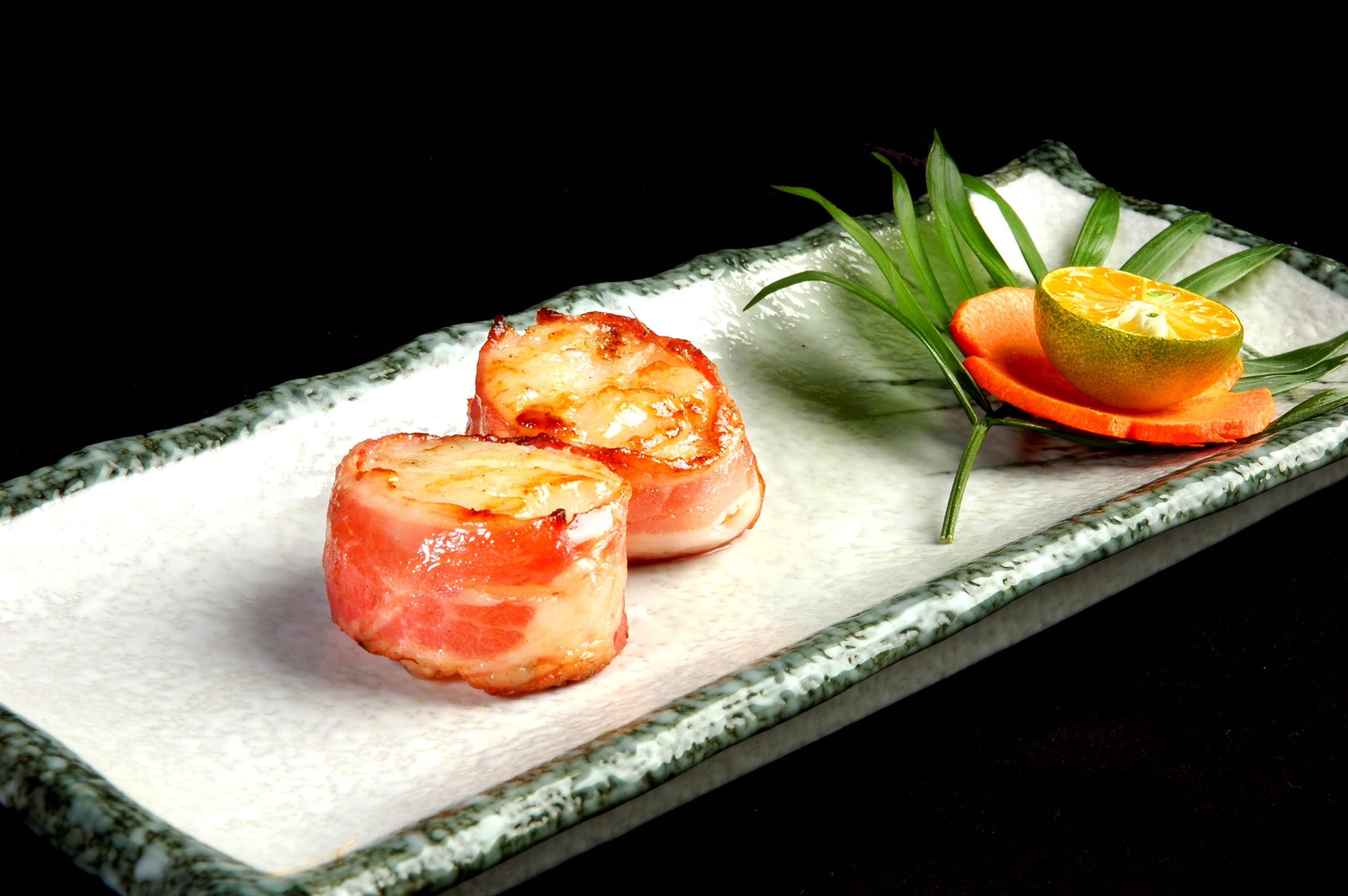 這張照片是兩片用培根包裹的扇貝，擺放在一個白色瓷盤上。