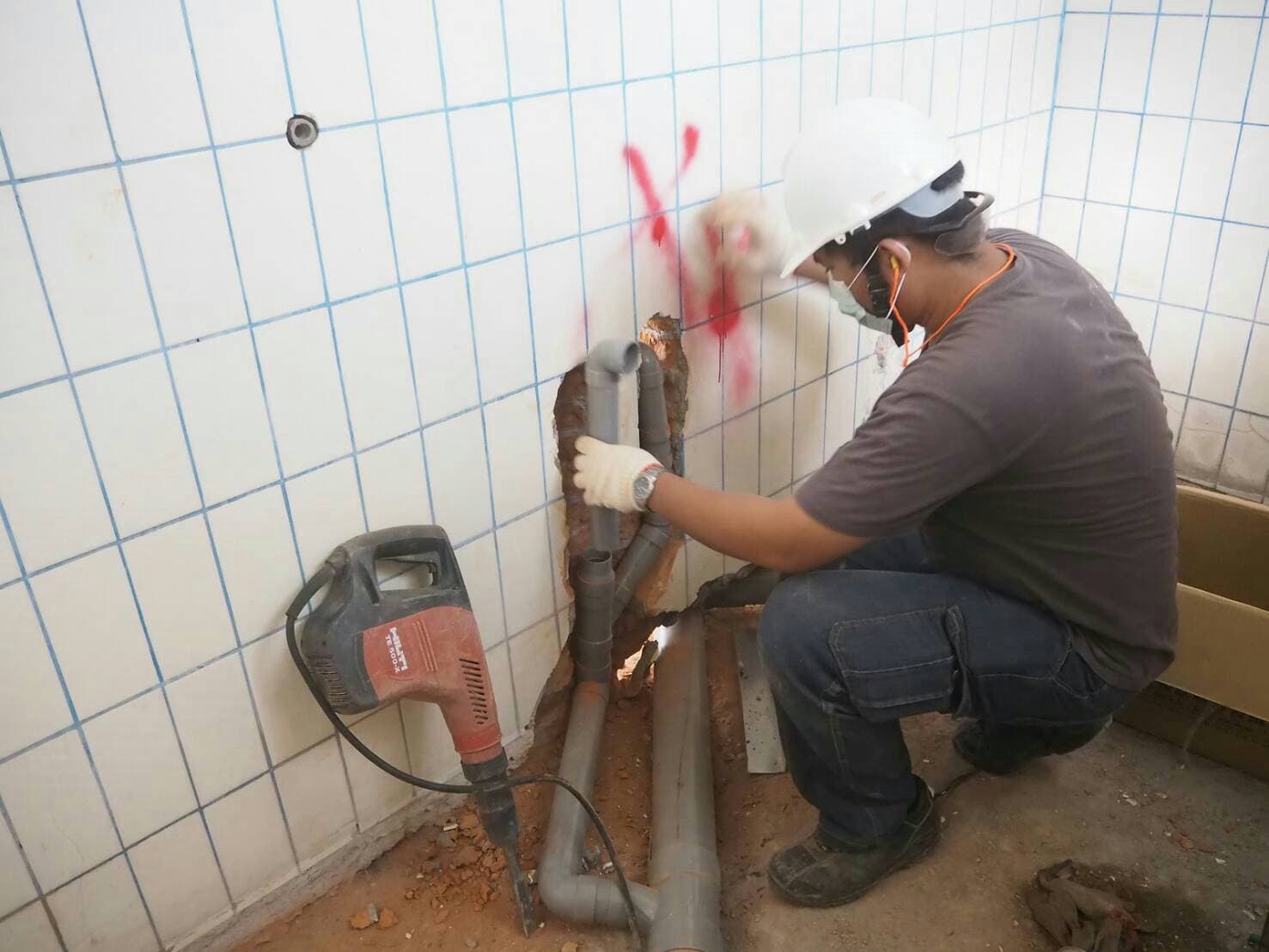 1) 照片顯示一名戴著安全帽的男子正在使用電鑽，在瓷磚牆上鑽孔