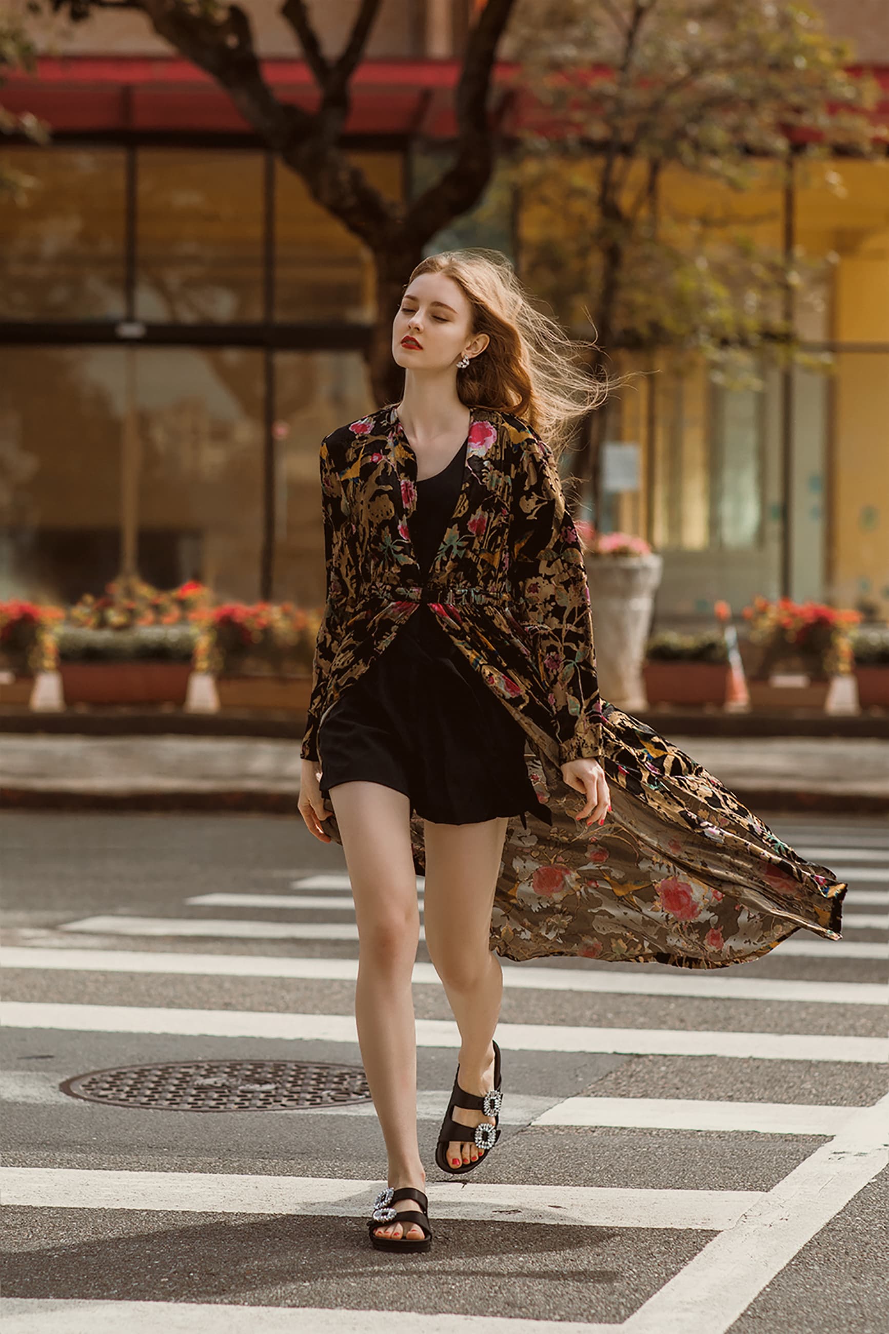 這張「一位女性走在斑馬線上的照片」是，她穿著黑色短褲和印花外套，正在過馬路，背景是繁華的街道。