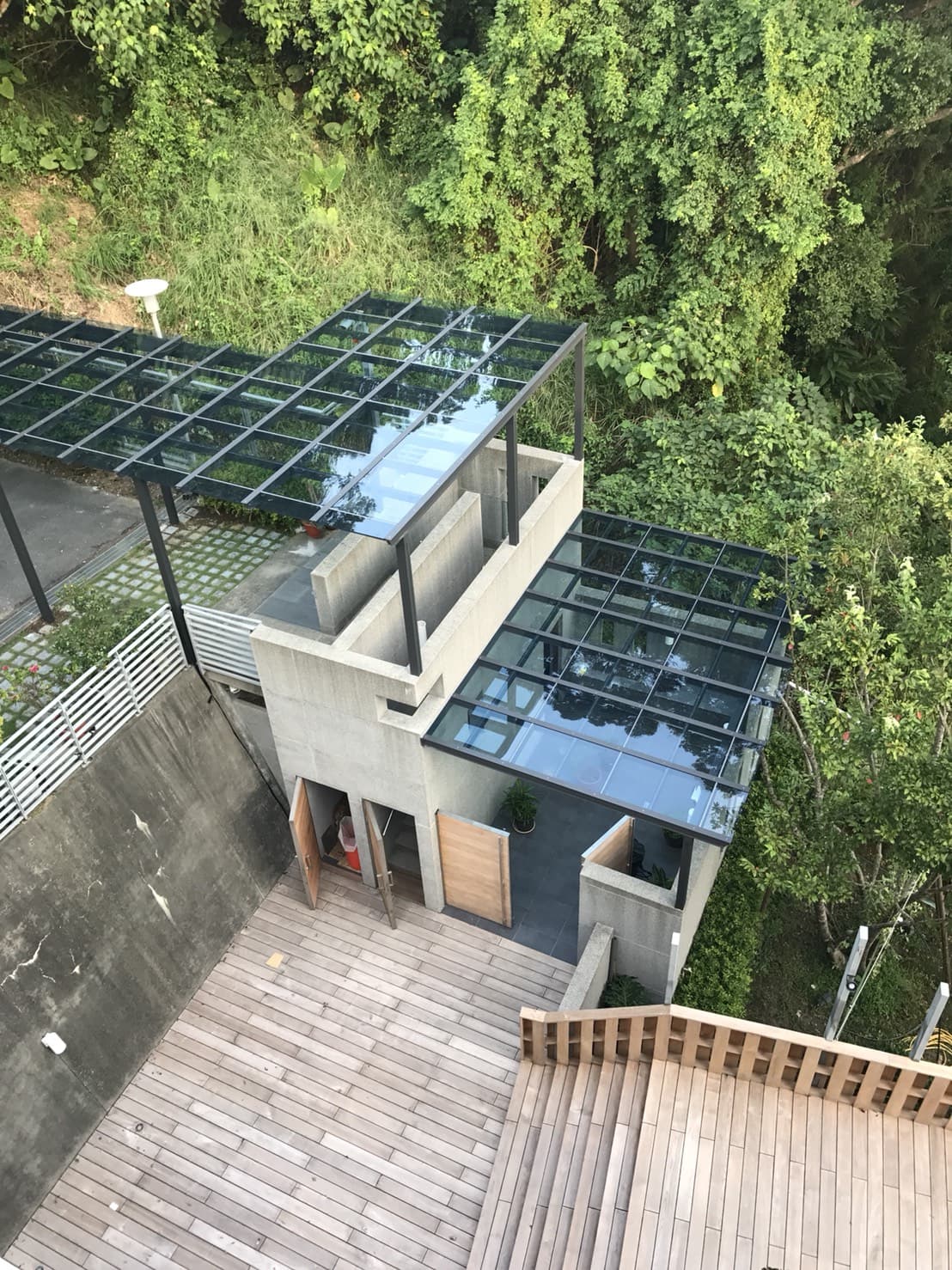 這張「現代建築」的照片是一個有玻璃屋頂的建築，建築旁邊有一個木質平臺，周圍被綠色的植物包圍。