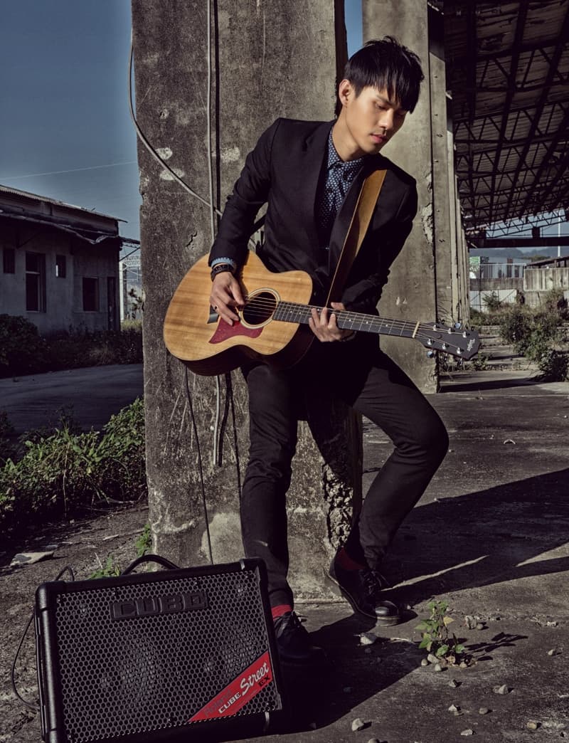 這張照片是一個年輕人拿著一把吉他站在牆壁旁，他看起來很專注在音樂上，他的表情很認真，他的手指正輕輕地按著吉他弦。  他背後有一臺音響，暗示著他即將要演奏音樂，這張照片傳達了音樂的力量和年輕人對音樂的熱情。