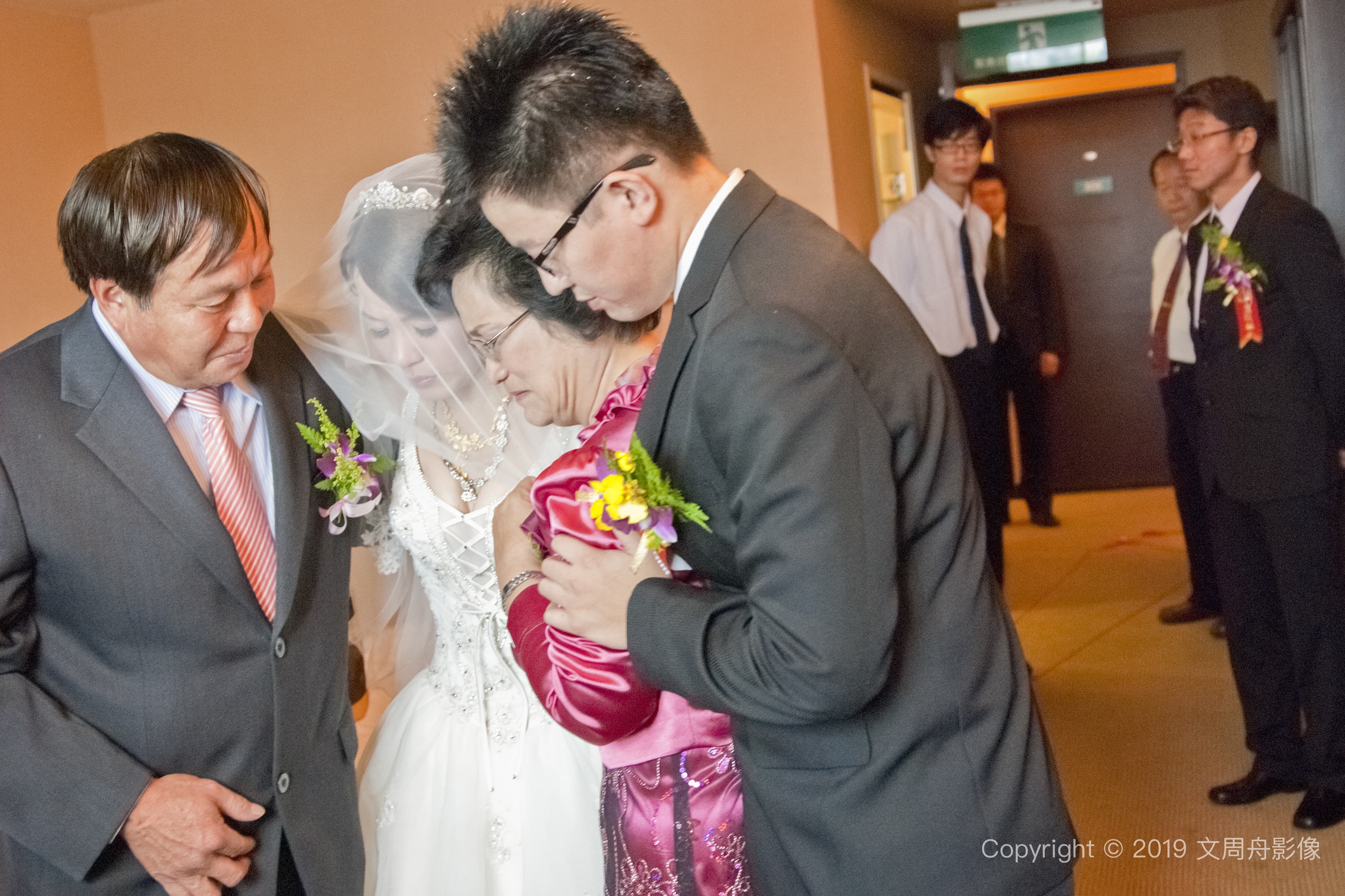 這張照片是一對新人正在舉行婚禮，新娘穿著婚紗，新郎穿著黑色西裝，他們正在交換戒指。新郎的右手拿著戒指，新娘的左手伸向新郎，準備戴上戒指。