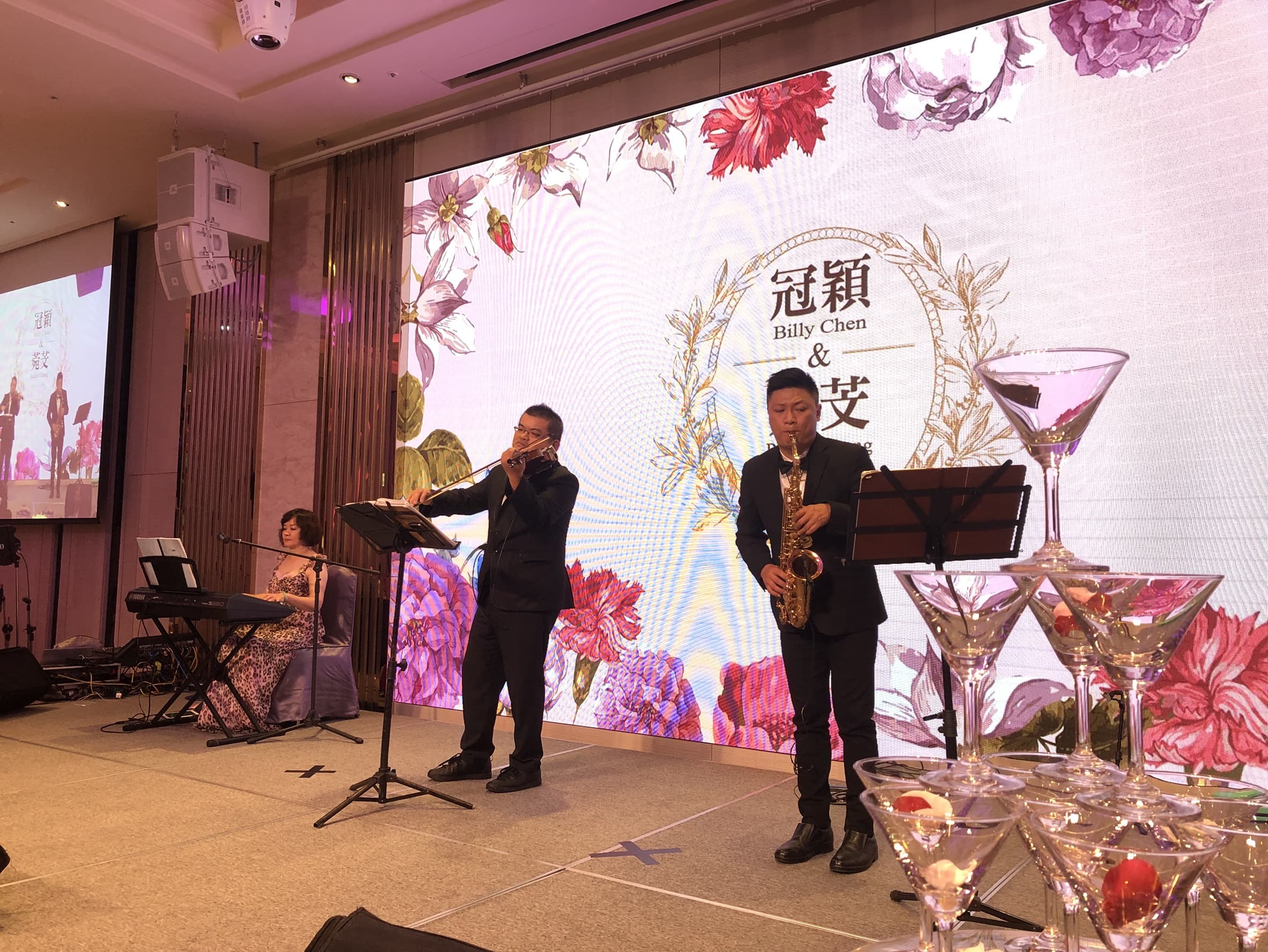 這張照片是一場婚禮現場，其中最重要的是舞臺上方的背景板，上面寫著新人的名字「冠穎」和「安」。