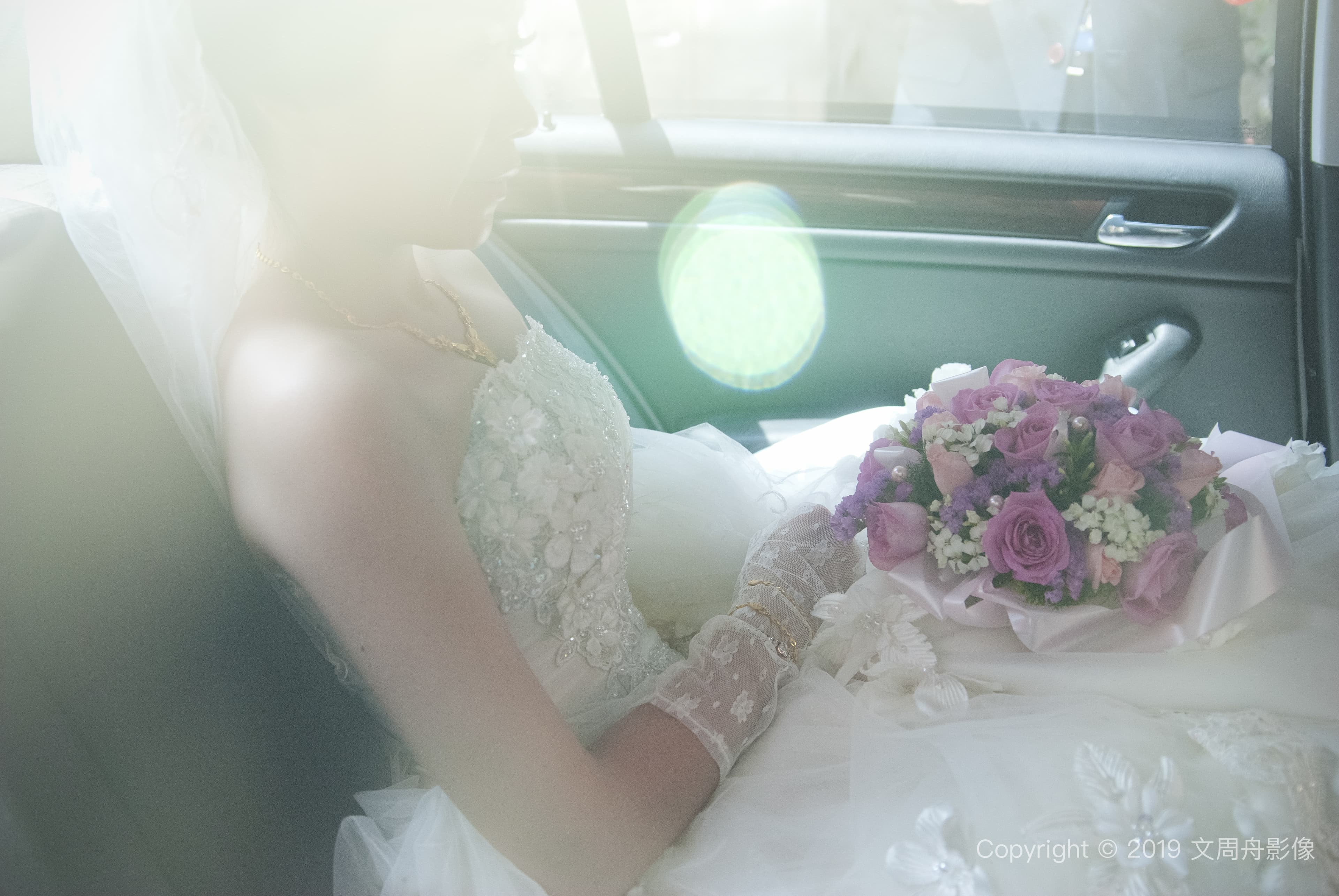 這張照片是一名身穿婚紗的女子坐在車裡，她手拿著一束紫色和白色的鮮花，眼神充滿幸福和期待。