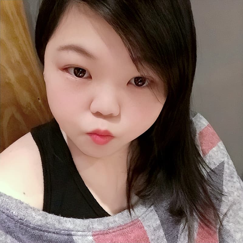 這張照片是一個年輕的女性自拍。她的頭髮烏黑亮麗，垂在她的臉上，遮住了部分臉孔。她穿著一件灰色和紅色的條紋毛衣，她的眼神充滿著自信和活力。