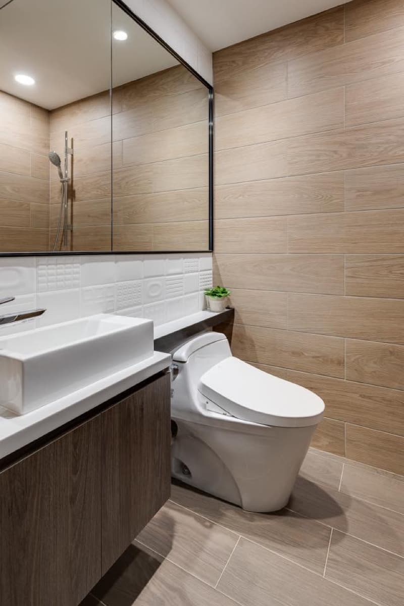 1) 照片顯示一個現代化、簡約的浴室，配備白色馬桶、鏡子、水槽和木質櫃子