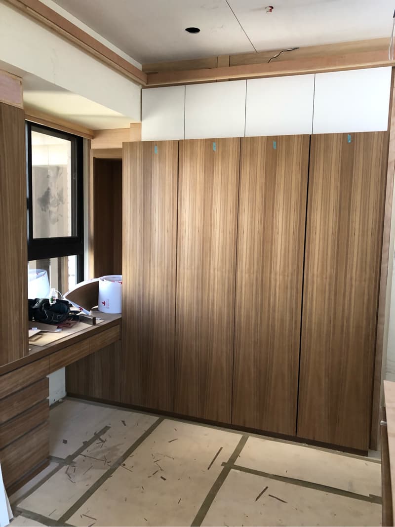 這張照片是房間裡的一個大型木質衣櫃。它由六個木板製成，並且有白色頂部。櫃子左側有一張木質書桌。