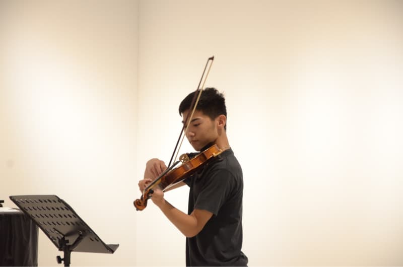 這張照片是一個年輕人正在演奏小提琴。他專注地看著琴弦，用弓演奏出優美的旋律。他的動作流暢自然，讓人感受到音樂的魅力。
