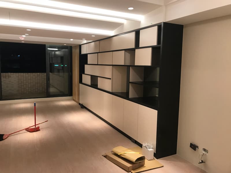 這張照片是一個現代化的客廳，最重要的是牆上的一個黑色和米色的開放式架子。架子上有許多隔層，可以放書、裝飾品和其他的物品。架子上面有燈，照亮了整個房間。