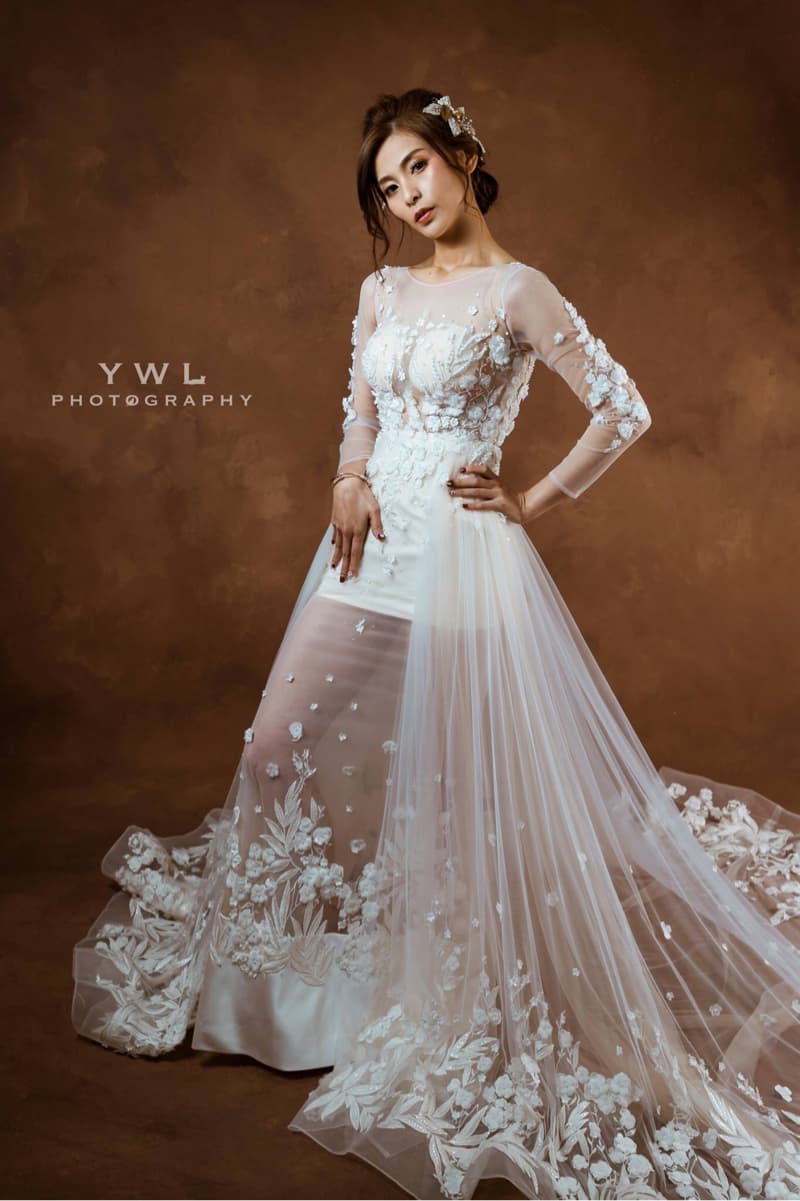 這張照片是一個美麗的新娘穿著一件精緻的婚紗，婚紗上滿是精緻的花朵刺繡，看起來非常華麗。