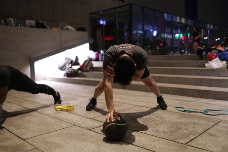 這張照片是一名男子在戶外做運動，他正使用一個藥球做伸展運動，看起來非常專注。
