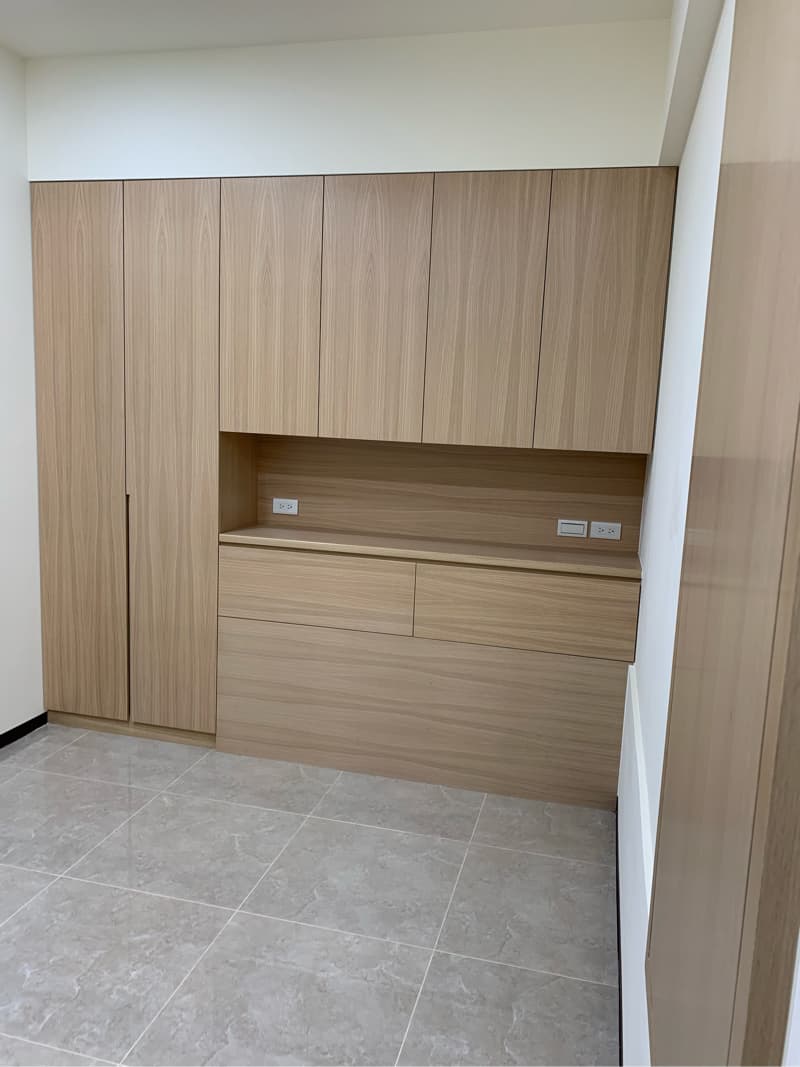 這張照片是一個現代化的房間，牆上裝有一個大型的木質櫃子，櫃子下方有抽屜和開放式架子，設計簡潔大方，整體空間看起來非常乾淨整潔。