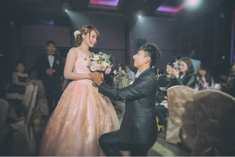 這張照片是一對新人正在舉行婚禮，新郎單膝跪地，向新娘求婚，新娘面帶微笑，接受了他的求婚。現場佈置簡潔，但充滿浪漫氣氛。