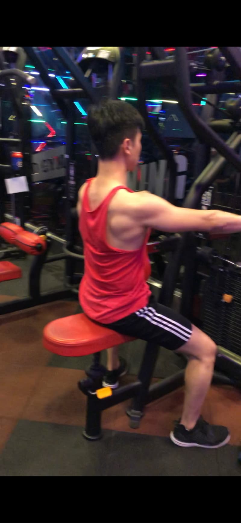 這張照片是一個年輕人在健身房裡使用器械鍛鍊，最重要的是他正在使用拉力器鍛鍊背部肌肉。