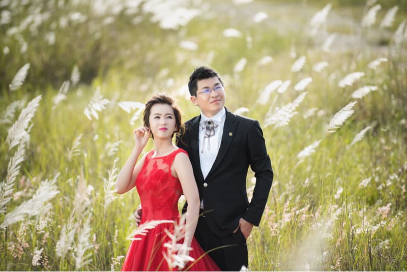 這張照片是一對新人站在綠色的草地上，他們彼此依偎著，男生穿著黑色西裝，女生穿著紅色禮服。