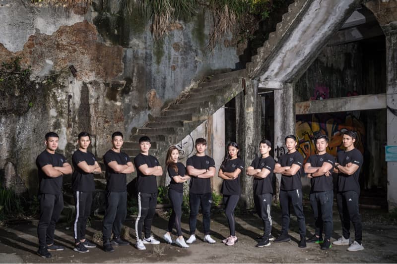 這張照片是一群穿著黑色衣服的年輕人在廢墟前拍照。他們都面帶笑容，看起來很自信，並以堅定的眼神凝視著鏡頭。這張照片傳達出團隊合作和堅定的精神。