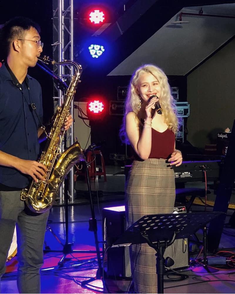 這張照片是一對男女在台上表演，女歌手正在唱歌，男歌手正在吹薩克斯風。他們正在台上表演，現場佈置簡樸，卻充滿活力。