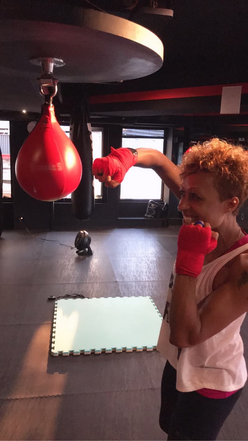 這張照片是一個拳擊訓練場，畫面中一位女性拳擊手準備揮拳攻擊掛在吊架上的紅色沙包。