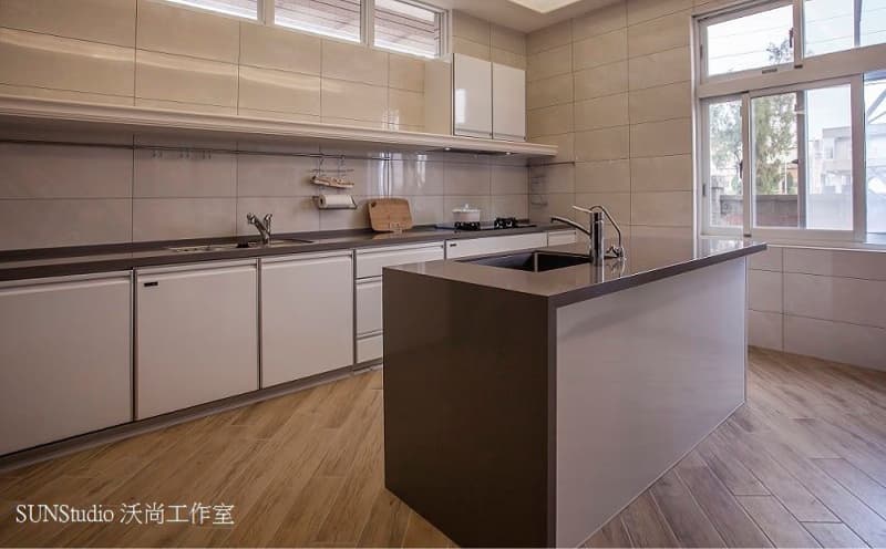 這張照片是一間現代化的廚房,照片中最主要的部分是廚房中央的白色中島,中島上有黑色的石英石檯面,檯面上有一個水槽和水龍頭。