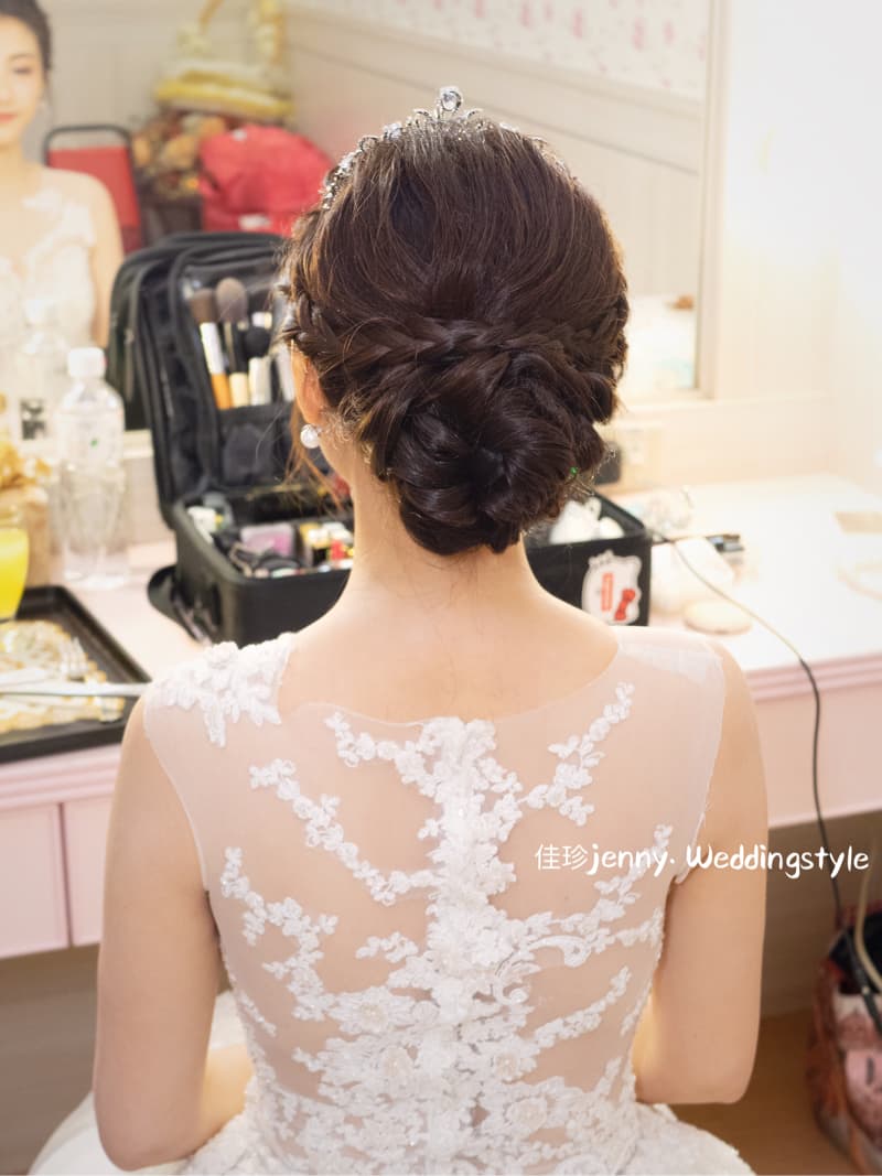 這張「新娘婚禮造型」的照片是一個新娘在化妝臺前，她穿著一件蕾絲婚紗，頭上戴著皇冠，頭髮做了一個編髮造型。