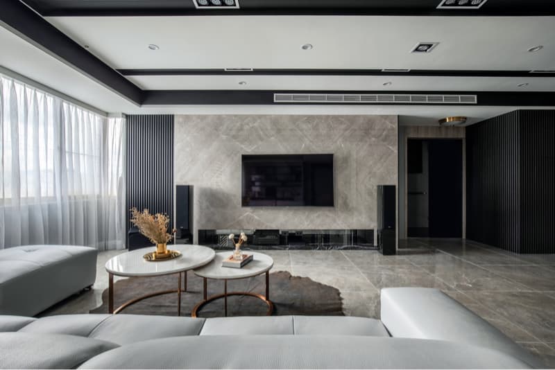 這張照片是一個現代化的客廳，中間有兩張圓形茶几，一張白色沙發，以及一面白色的牆上掛著一臺大電視。