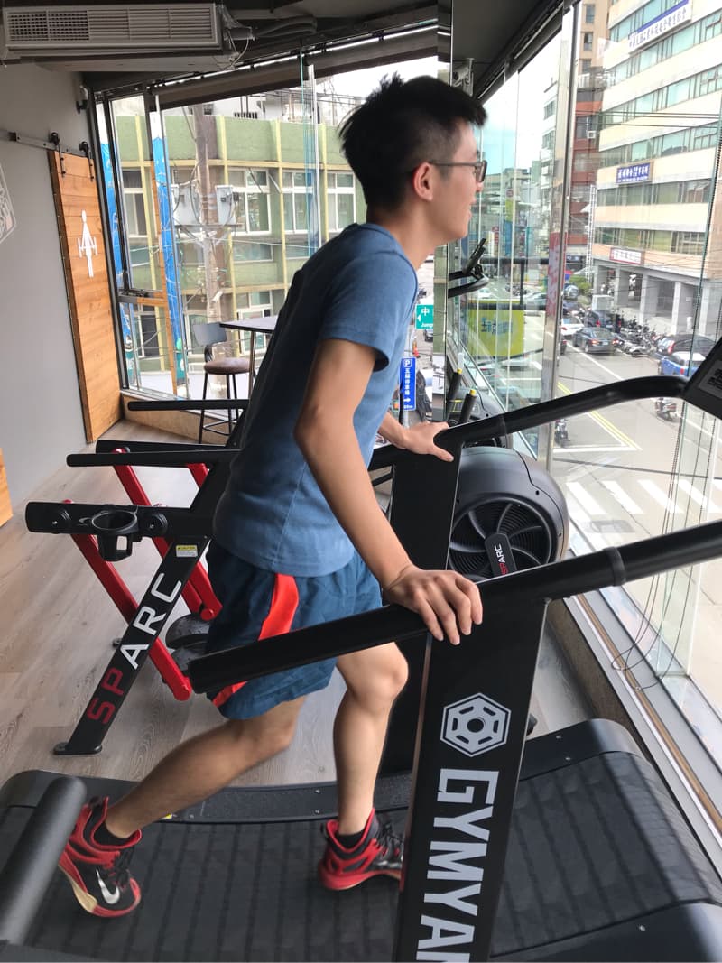 這張照片是一個男人在使用健身器材跑步。 他正踏上跑步機，並握住扶手。 他的動作看起來十分專注。