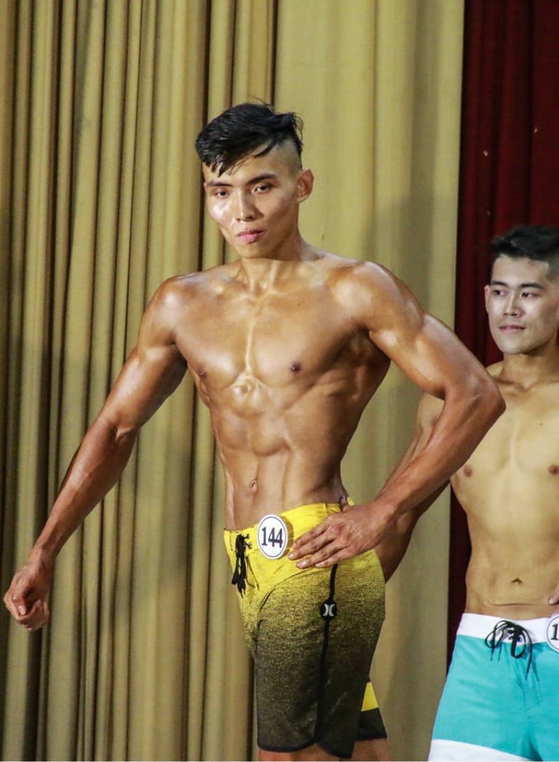 這張照片是一個健美比賽,照片中有一個健美運動員,他正在展示他的肌肉。他穿著黃色的比基尼,並在舞臺上展現他的健美身材。