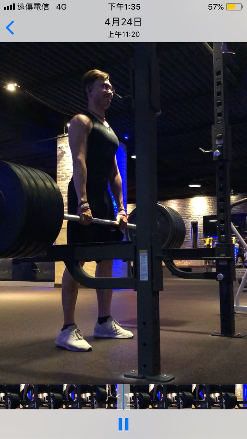 這張照片是一個男人在健身房舉重。他正準備從地面上舉起一個槓鈴。他正在使用一個槓鈴架來幫助他舉起重量。