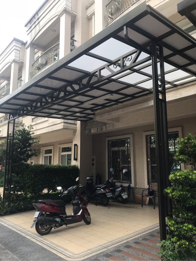 1. 照片顯示一棟房屋的入口處，有一個鐵製的遮雨棚，以及停放著一輛摩托車和兩輛機車