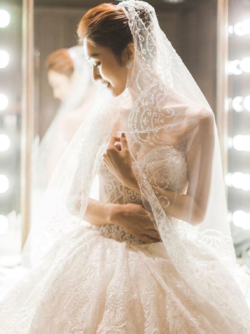 這張「新娘穿著白色婚紗，戴著頭紗，手拿著婚紗裙襬」的照片是。