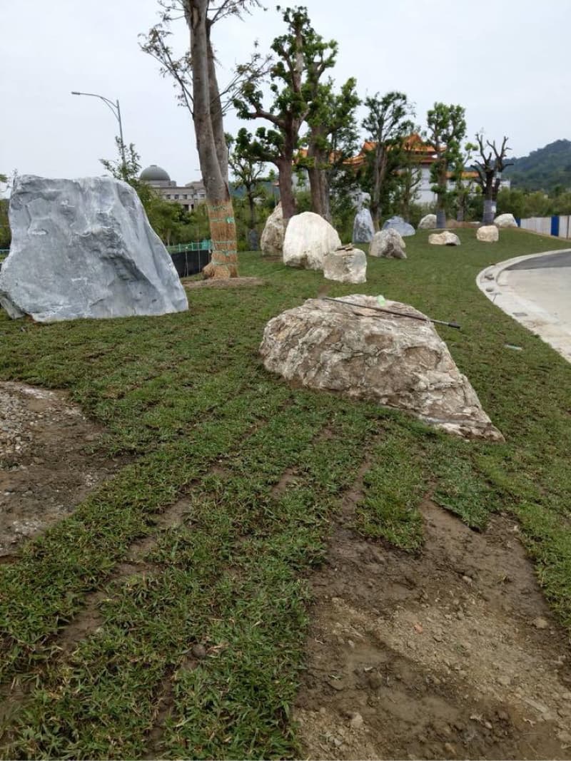 這張照片是一片綠色的草坪，上面放著許多大小不一的石頭，草坪旁有泥土和一些碎石。