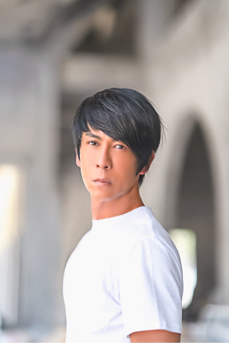 這張照片是一個穿著白色T恤的年輕男子，他面無表情地看著鏡頭。