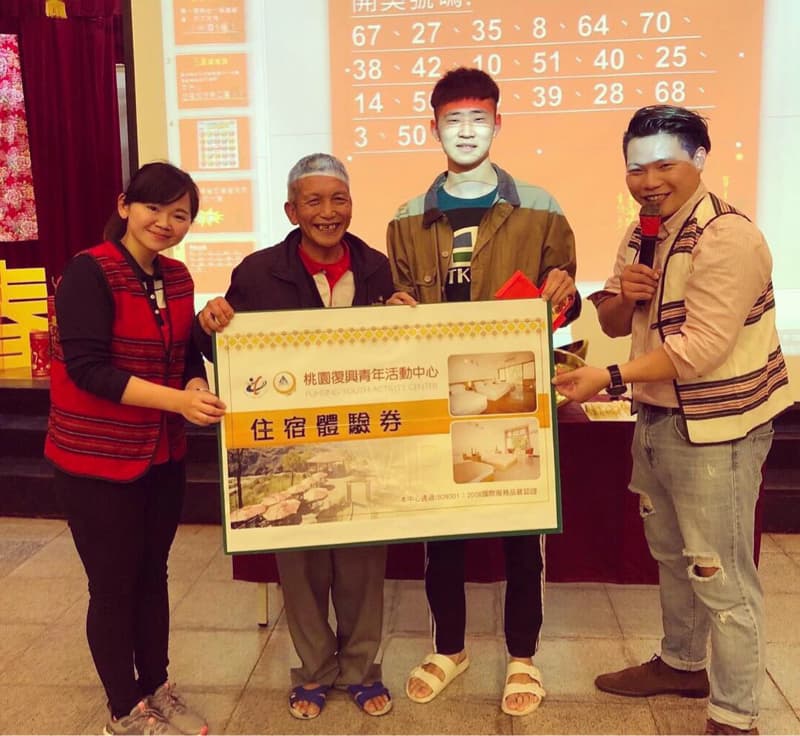 這張照片是一個頒獎典禮，一個年輕人拿著「住宿體驗券」獎狀，另外兩位則是頒獎人。