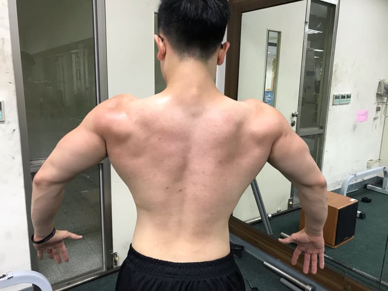 這張「健美運動員」的照片是一個肌肉發達的男子，他站在鏡子前，背對著鏡頭，展示著他強健的背部肌肉。