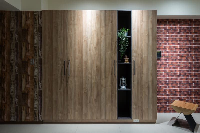 這張照片是一個木製的衣櫃，衣櫃的門上裝有黑色的把手，在衣櫃的中央有一個黑色的開放式櫃子，櫃子裡擺放著一些裝飾品，像是植物、燈籠和一個咖啡研磨器。