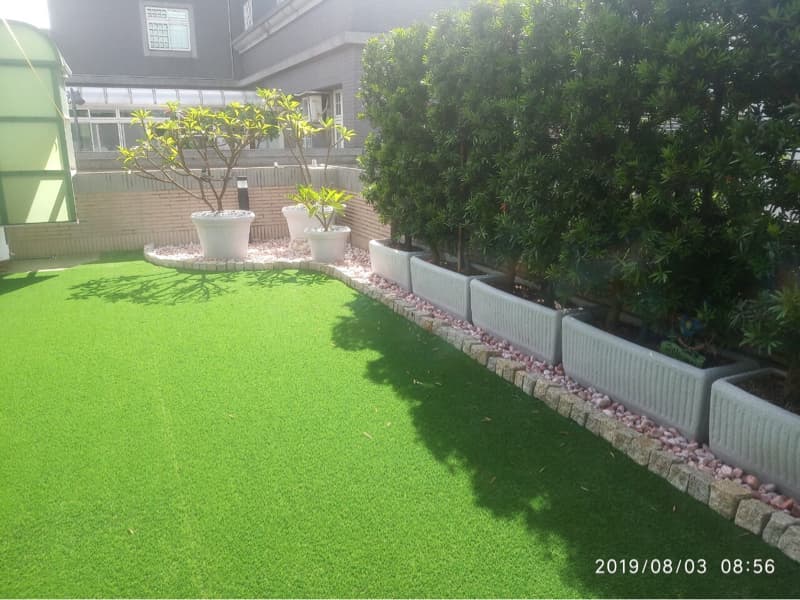 這張照片是一片綠色的草坪，草坪上鋪滿了紅色的石頭，還有一些盆栽。